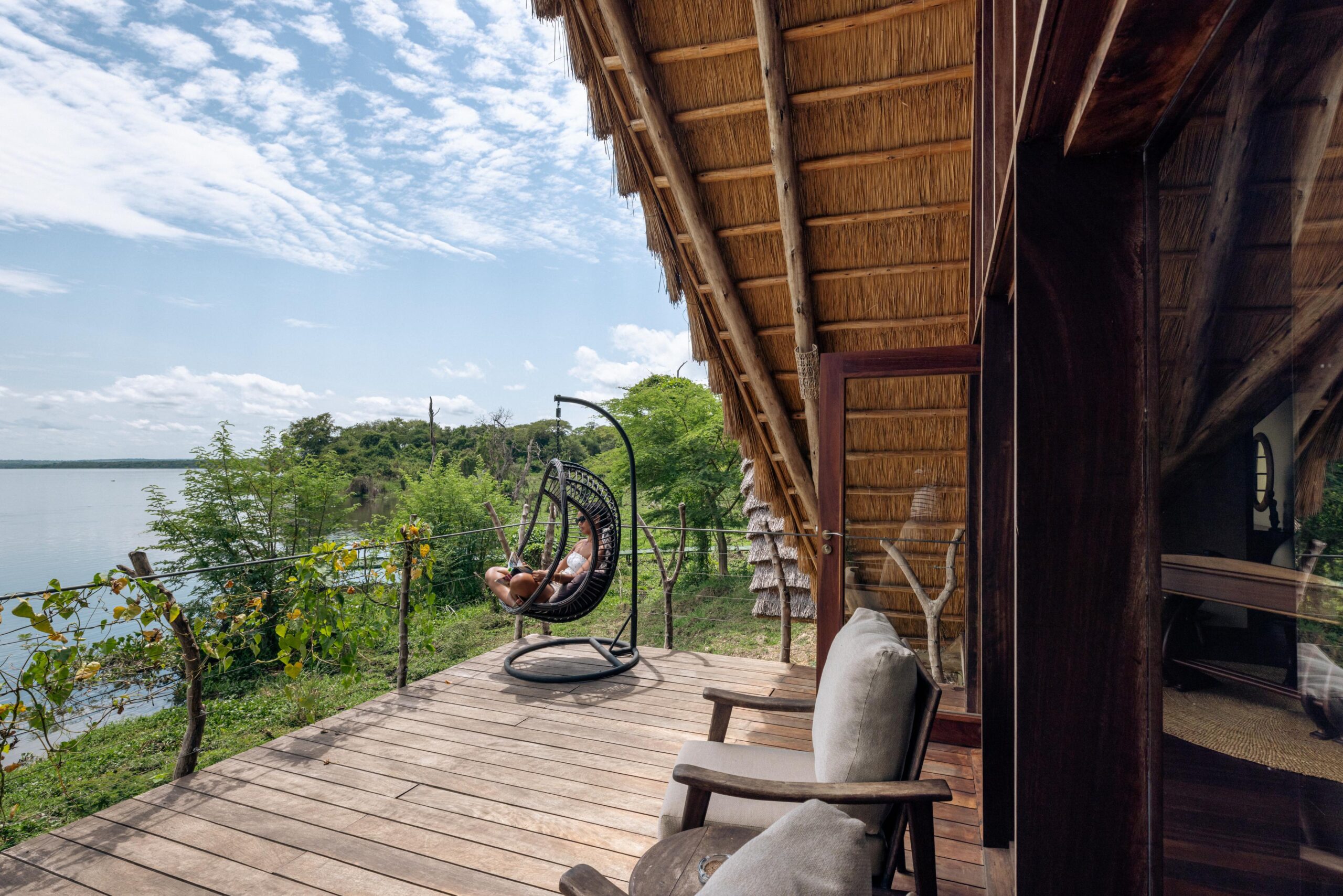 Private wooden deck at Nile Safari Lodge’s Deluxe Banda, offering a comfortable seating area, a hanging chair, and panoramic views of the Nile River and lush landscapes.