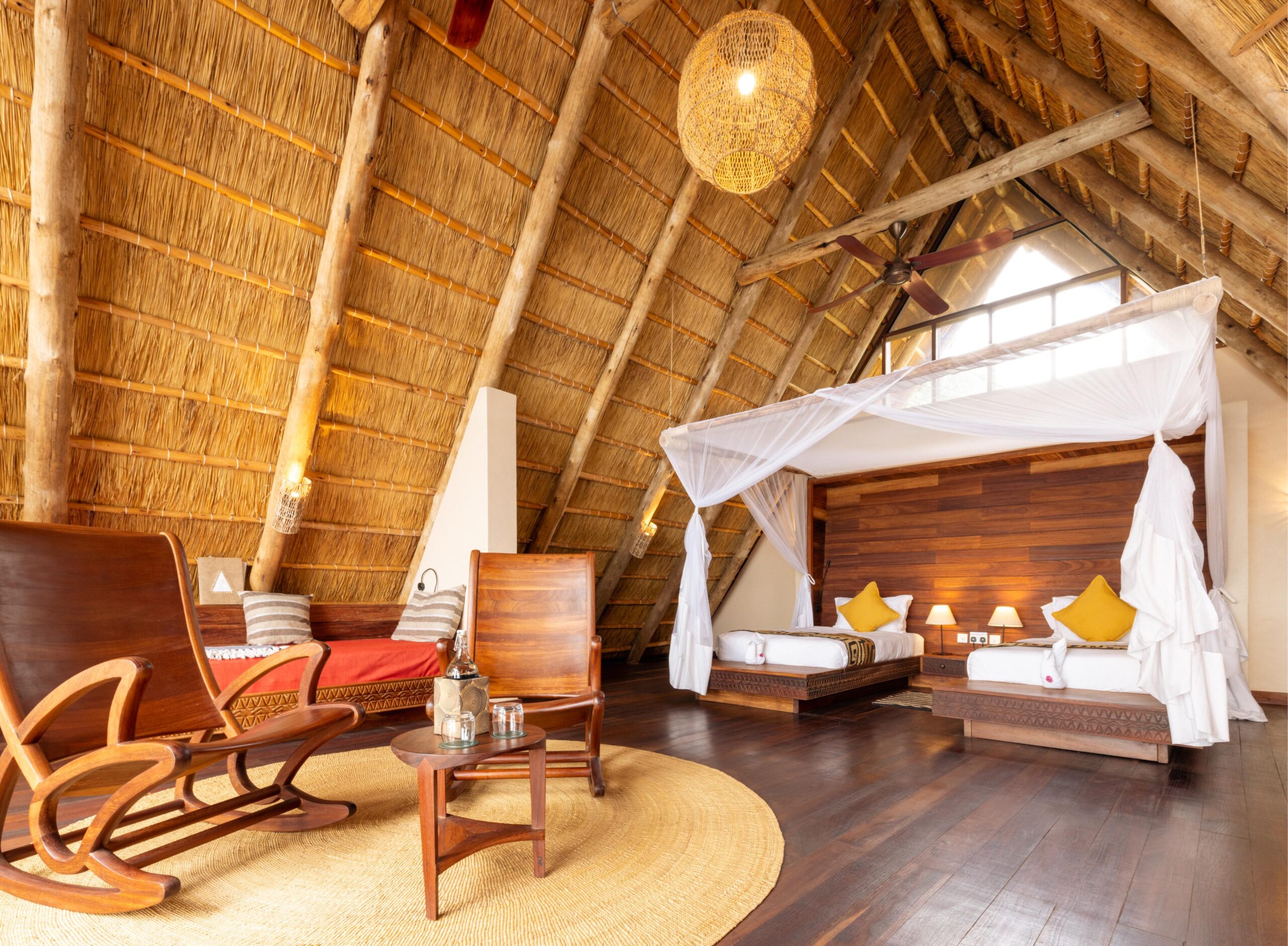 Spacious Deluxe Banda lounge at Nile Safari Lodge, Uganda, featuring handcrafted wooden furniture, a cozy seating area, and an open-plan design with traditional thatched roofing for a luxurious safari retreat.